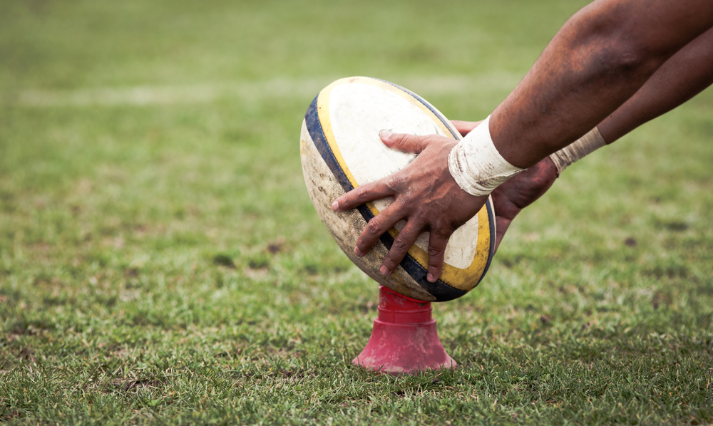 A rugby player placing a ball on the ground to kick it.