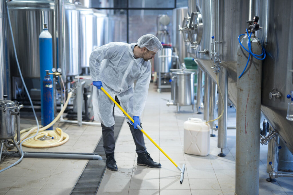 A worker in protective clothing diligently cleaning the floor of a modern food production facility, emphasizing the high standards of sanitation in the industry.