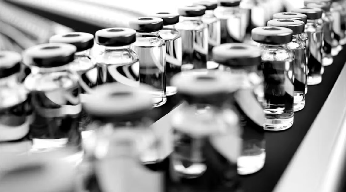 Close-up of pharmaceutical vials on a conveyor belt in a black and white image, symbolizing the precision and cleanliness in modern drug manufacturing.